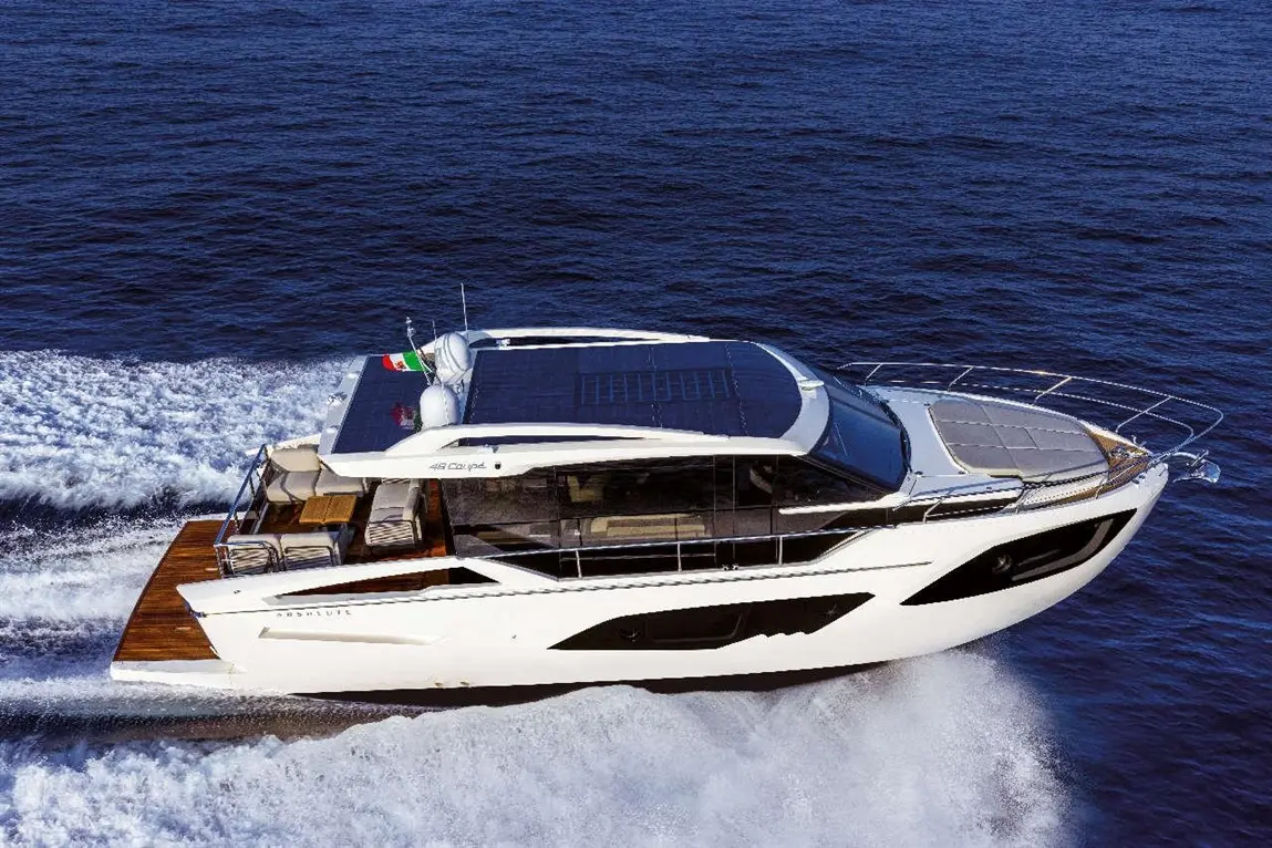Luxury yacht cruising through waves, featuring a solar panel on the roof and a sleek white design against a blue ocean.